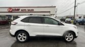White SUV parked in front of E-Z Loan Auto Sales on a cloudy, rainy day with other vehicles and the dealership sign in view.