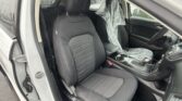 Front interior of a car showing black cloth seats, plastic seat cover on the passenger seat, and water droplets on the windows with open door frame visible.