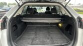 Open hatch shows a spacious SUV cargo area with a black rubber floor mat and rear seats upright, raindrops on windows in the background.
