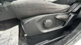 Close-up of a car front seat with fabric upholstery and a plastic protective bag on the seat, plus the manual adjustment knob nearby.