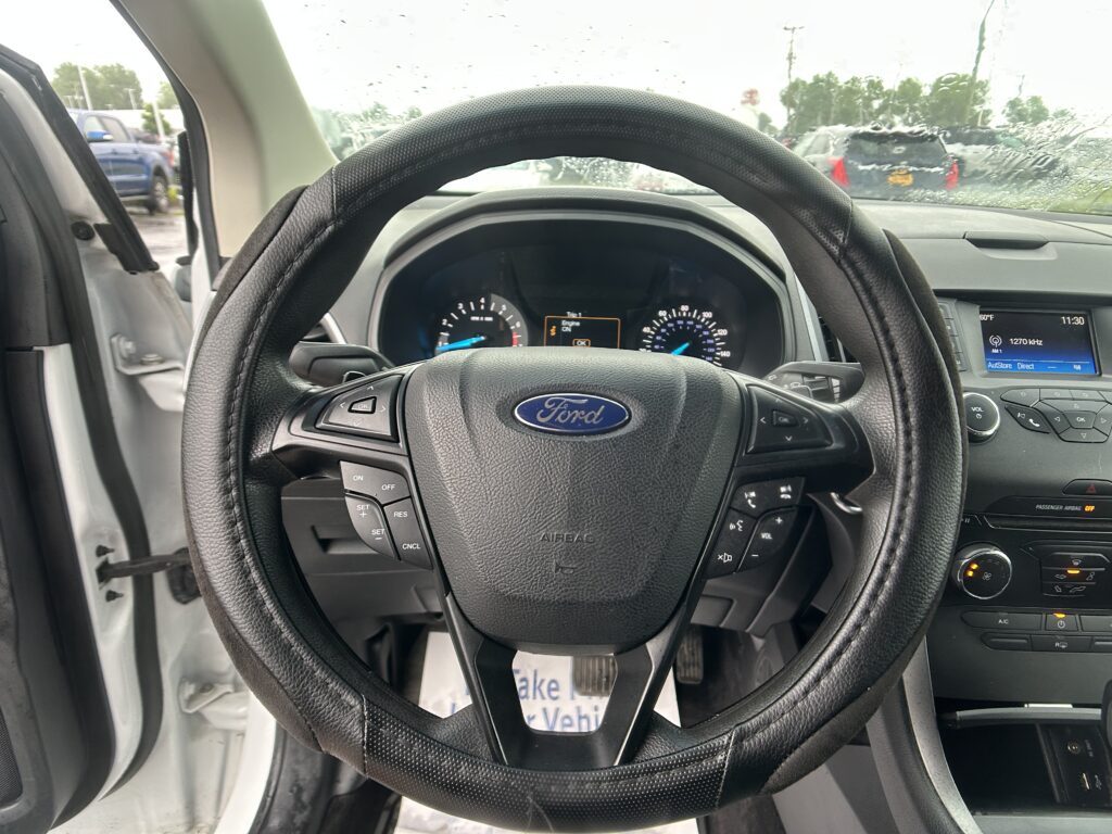 View from the driver's seat of a Ford with steering wheel center stage and rain-speckled windshield outside the car doors