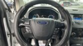 View from the driver's seat of a Ford with steering wheel center stage and rain-speckled windshield outside the car doors