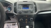 Interior view of a car dashboard with center console, gear shifter, and climate controls; raindrops on the windshield and a parking lot outside are visible.