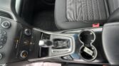 Center console area of a car interior showing the gear shifter, cup holders, and climate control panel near a black fabric seat.
