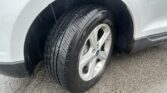 Close-up of a car tire and alloy wheel inside the wheel well, with raindrops on the silver body above.