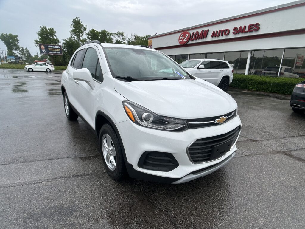 White Chevrolet SUV in the foreground at a rainy car dealership lot, EZ LOAN Auto Sales visible in the background.
