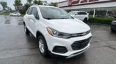 White Chevrolet SUV in the foreground at a rainy car dealership lot, EZ LOAN Auto Sales visible in the background.