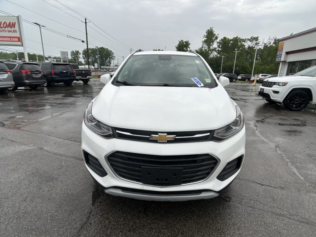Front view of a white Chevrolet SUV in a car dealership lot on a rainy day, with other vehicles in the background.