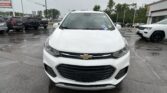 Front view of a white Chevrolet SUV in a car dealership lot on a rainy day, with other vehicles in the background.