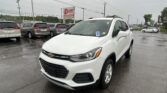 White Chevrolet SUV in a wet dealership lot with many minivans and an EZ LOAN sign in the distance.