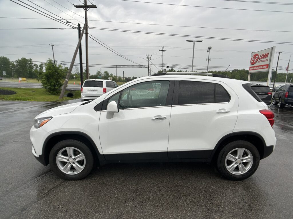 White SUV in a wet parking lot with other vehicles and a large EZ Loan Auto Sales sign in the background under cloudy skies.