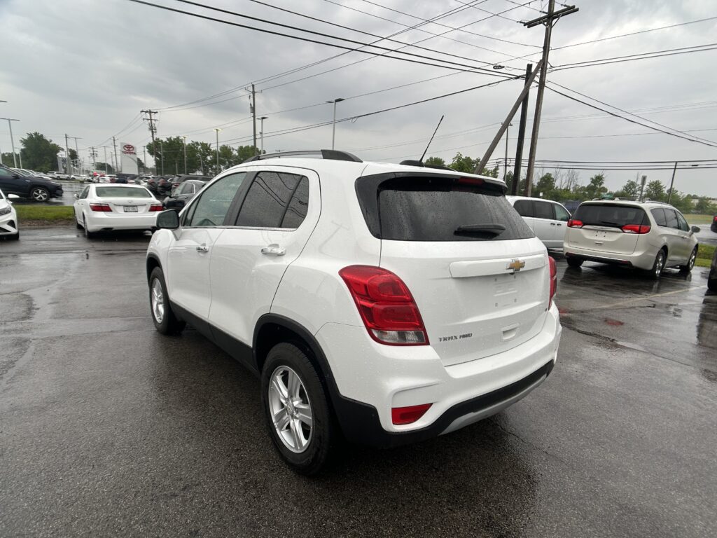 White Chevrolet SUV in a rainy dealership parking lot, close to the camera with other white vehicles in the background and wet pavement under an overcast sky.