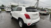White Chevrolet SUV in a rainy dealership parking lot, close to the camera with other white vehicles in the background and wet pavement under an overcast sky.