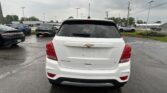 Rear view of a white Chevrolet Trax SUV in a wet parking lot with other vehicles and an overcast sky.