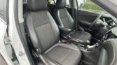 Front interior of a car showing two black, stitched leather seats and the dashboard/window with raindrops outside.