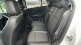 Interior of a car back seat with black leather seats and orange stitching, three seats and headrests, rain on the windows outside.