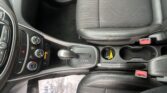 Close-up of a car interior showing the gear selector, center console, and black seat with orange stitching tailing the passenger area.