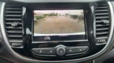 Car rear camera display on the vehicle dashboard showing orange parking guidelines over a wet parking lot behind the car.