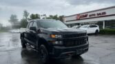 Black pickup truck parked in a wet parking lot near an auto sales storefront under a cloudy sky.",