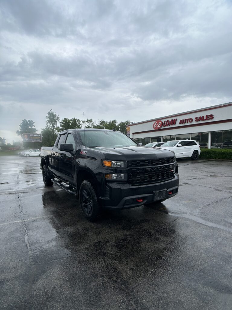 Black pickup truck parked in a wet parking lot near an auto sales storefront under a cloudy sky.",