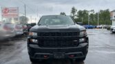 Front view of a black pickup truck in a car dealership lot on a rainy day.