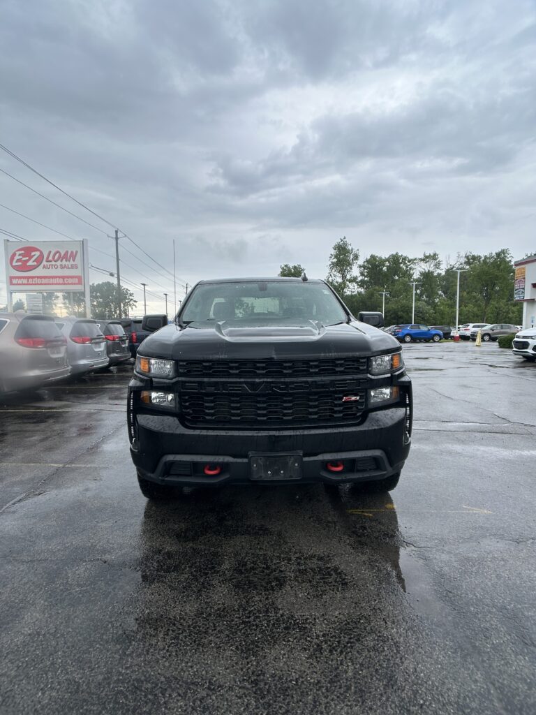 Front view of a black pickup truck in a car dealership lot on a rainy day.