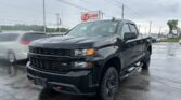 Black pickup truck parked in a wet car lot with an EZ Loan Auto Sales sign in the background.