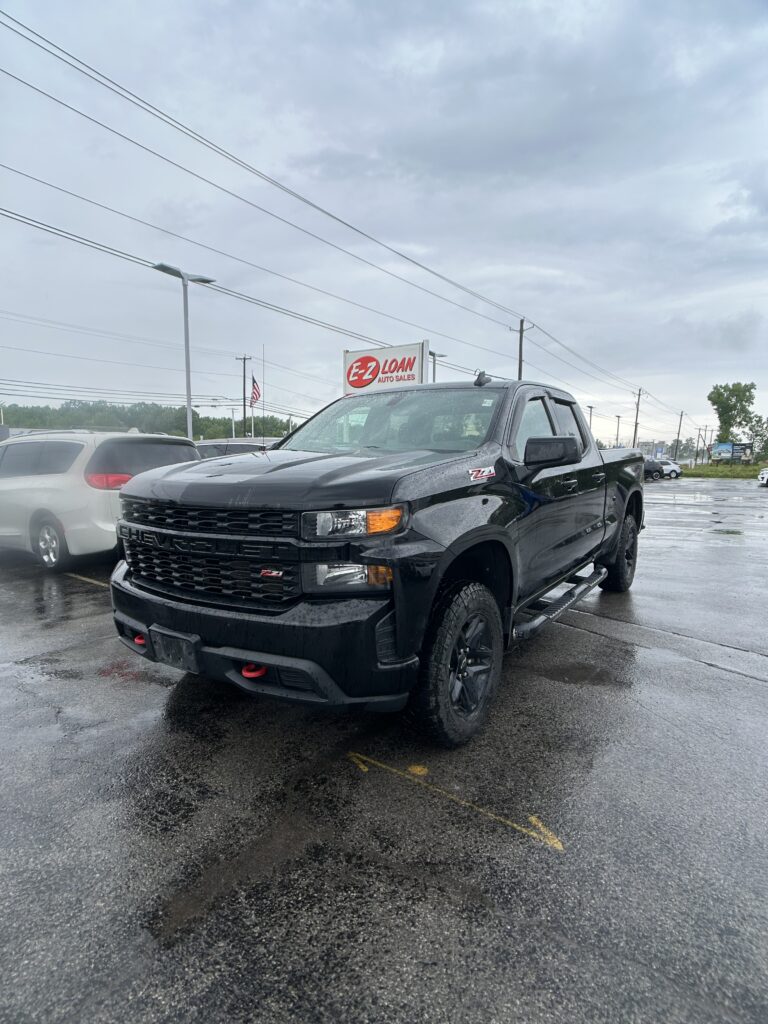 Black pickup truck parked in a wet car lot with an EZ Loan Auto Sales sign in the background.