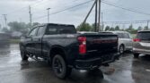 Black Chevrolet Silverado pickup parked in a wet lot with overhead power lines and stormy sky in the background.