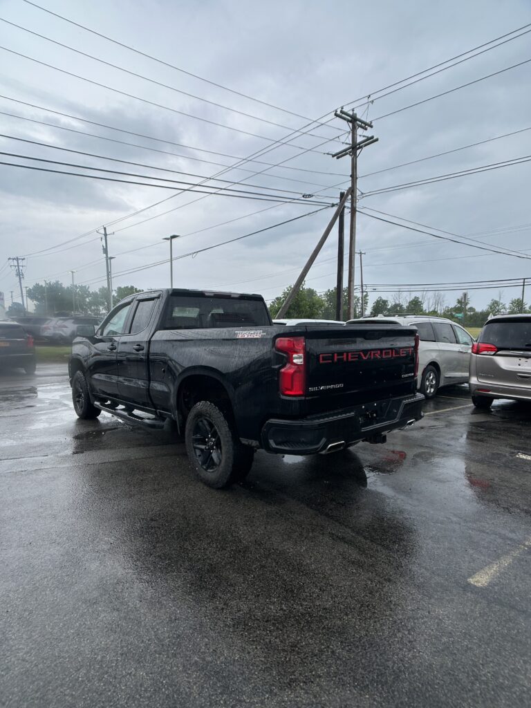 Black Chevrolet Silverado pickup parked in a wet lot with overhead power lines and stormy sky in the background.