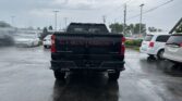 Rear view of a black Chevrolet Silverado pickup with red lettering, parked in a wet dealership lot on a cloudy day.