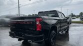 Rear three-quarter view of a black Chevrolet Silverado pickup in a rainy dealership lot, with power lines overhead and wet pavement.