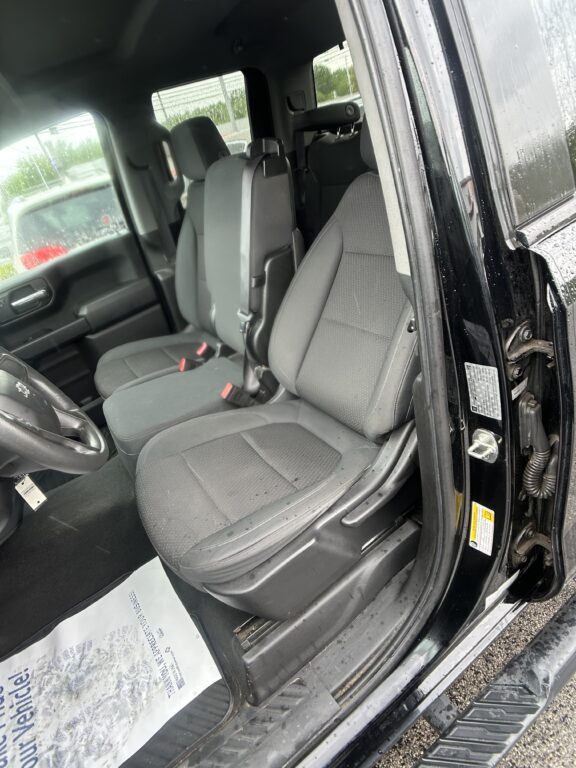 Interior of a black pickup truck with gray cloth seats, driver’s seat and front passenger seat visible, door open.