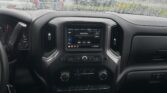 View from the driver seat of a pickup with a rainy windshield; dashboard and center touchscreen showing radio controls visible in the foreground