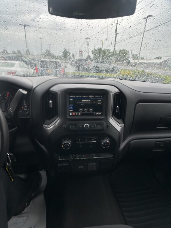 View from the driver seat of a pickup with a rainy windshield; dashboard and center touchscreen showing radio controls visible in the foreground
