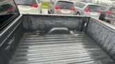 View from inside a pickup truck bed looking toward a row of silver and gray minivans parked in a car lot on a rainy day.