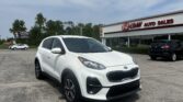 White Kia SUV parked in front of EZ Loan Auto Sales storefront on a sunny day.