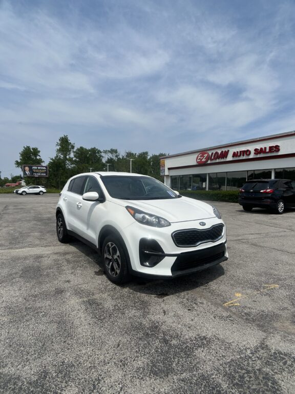 White Kia SUV parked in front of EZ Loan Auto Sales storefront on a sunny day.
