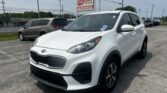 White Kia SUV in a dealership lot with an E-Z LOAN Auto Sales sign in the background.