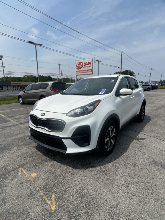 White Kia SUV in a dealership lot with an E-Z LOAN Auto Sales sign in the background.