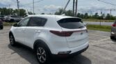 White Kia Sportage SUV parked in a lot with utility poles and power lines overhead, blue sky in the background.