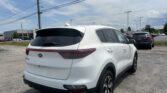 Rear three-quarter view of a white Kia SUV in a parking lot under a blue sky with power lines above.