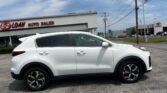 White SUV parked in a car dealership lot with 'E-Z LOAN AUTO SALES' sign in the background and a Toyota dealership nearby.