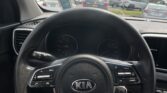Close-up view of a Kia steering wheel from the driver’s seat, with a busy parking lot visible through the windshield.