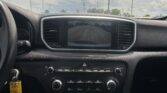 Interior of a car dashboard with a rear-view camera display showing parking guidelines (yellow/red/green lines) in a dealership lot viewable through the windshield.