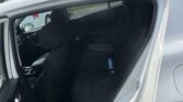 Open rear passenger door of a white SUV, showing black fabric seats and a blue water bottle on the back seat, with a parking lot outside.