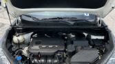 Under-hood view of a Kia with torn hood liner exposing engine compartment and damaged insulation patch on the underside of the hood.