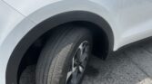 White SUV with the hood open, showing the front-left wheel and fender in a parking lot.