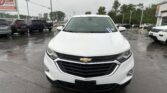 Front view of a white Chevrolet SUV in a car dealership lot on a rainy day, with wet pavement and other vehicles in the background.