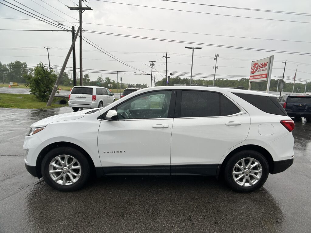 White Chevrolet Equinox parked in a wet parking lot with power lines and a sign in the background on a rainy day.